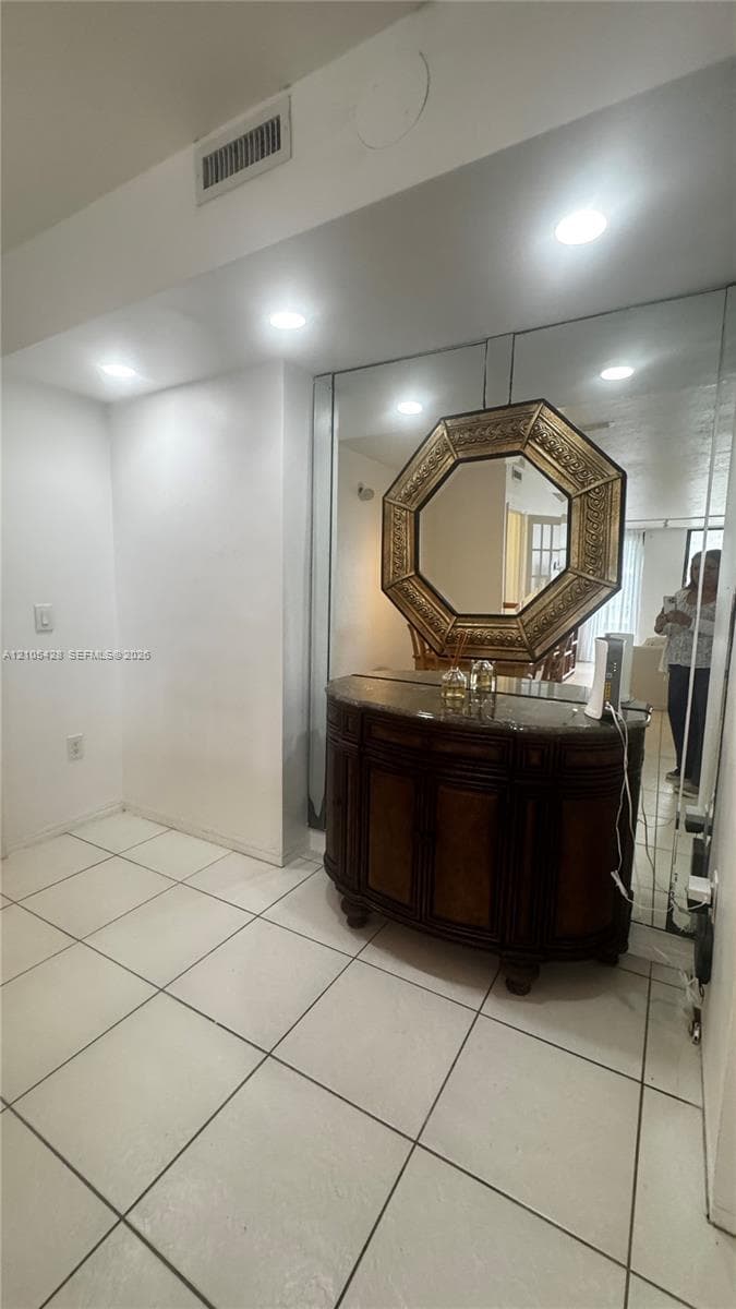 Recessed lighting illuminates the space, featuring large square floor tiles and white walls