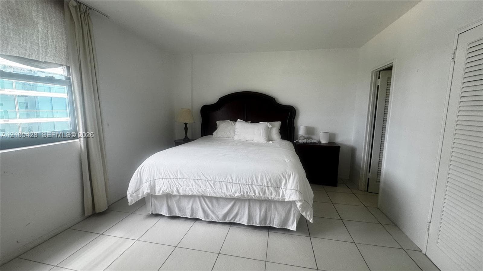 White tile flooring, white painted walls, and a louvered door
