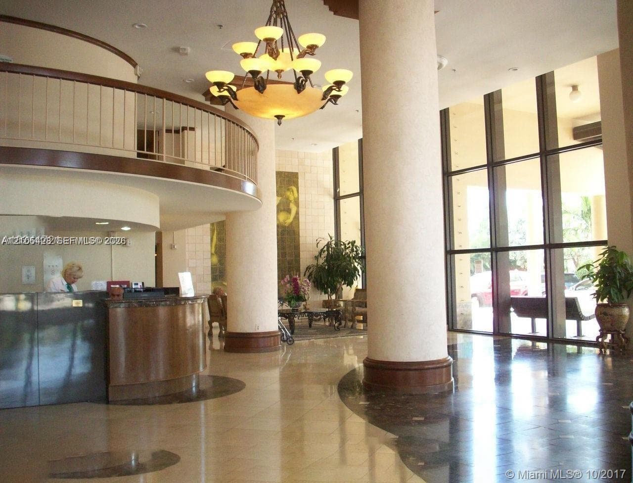 Multi-story building featuring individual balconies, a ground-level swimming pool, and surrounding mature palm trees