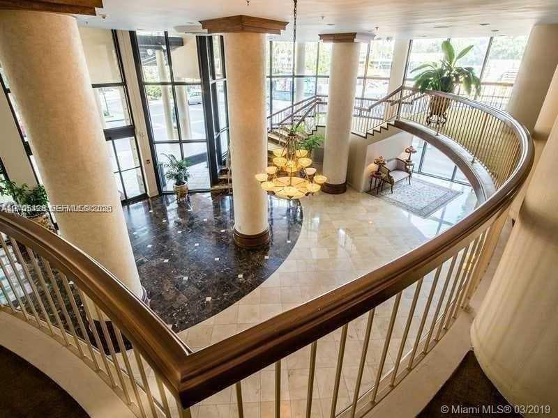 Two-story foyer featuring a grand chandelier, curved architectural balcony, tall window panels, and polished flooring with circular inlay