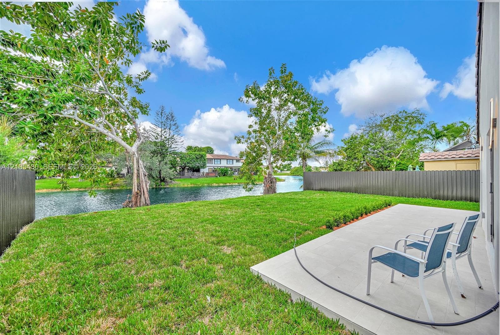 Rear yard featuring a paved patio, manicured lawn, perimeter fencing, and water frontage