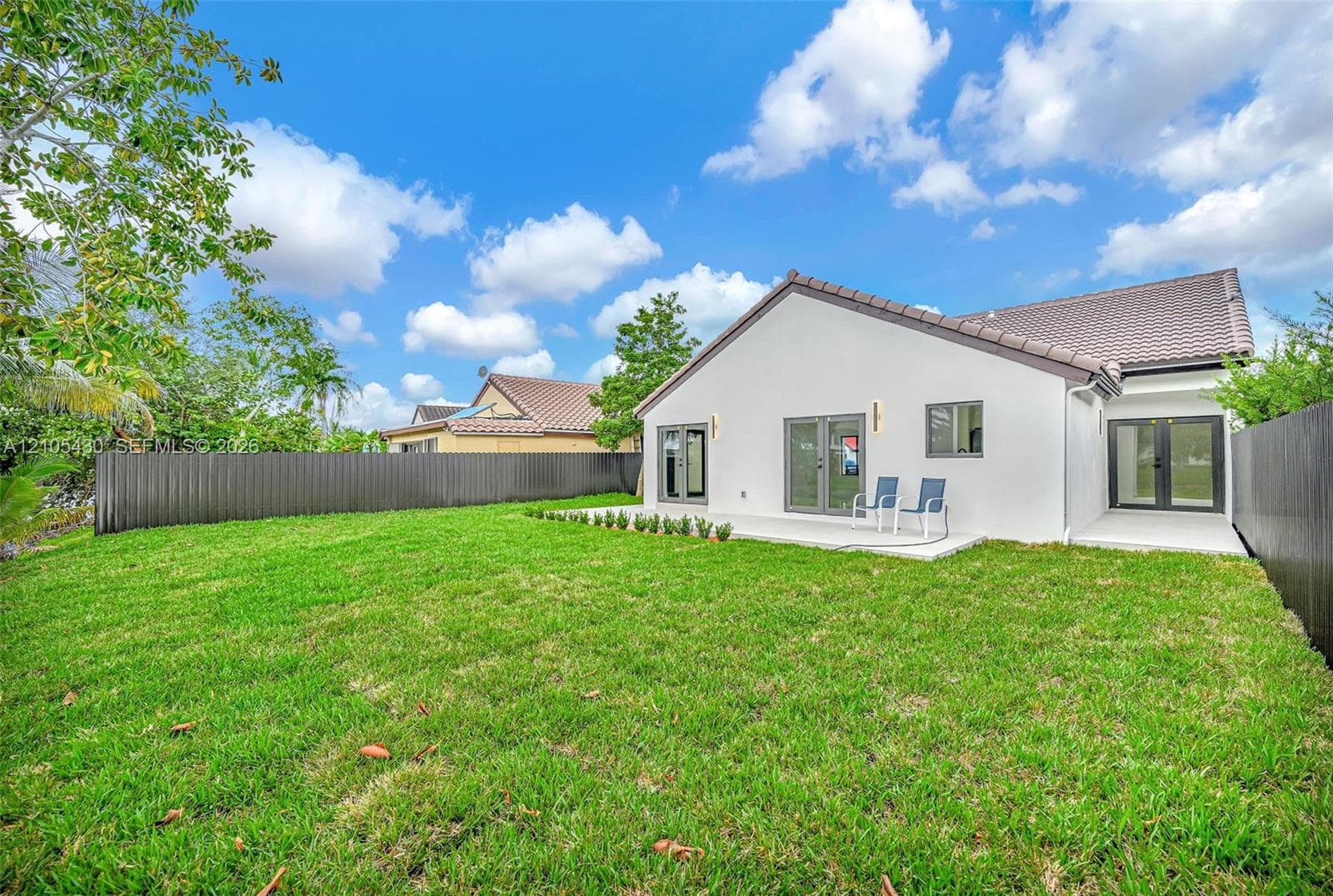 Backyard featuring a spacious lawn, concrete patio, perimeter privacy fencing, and double-door rear entryways