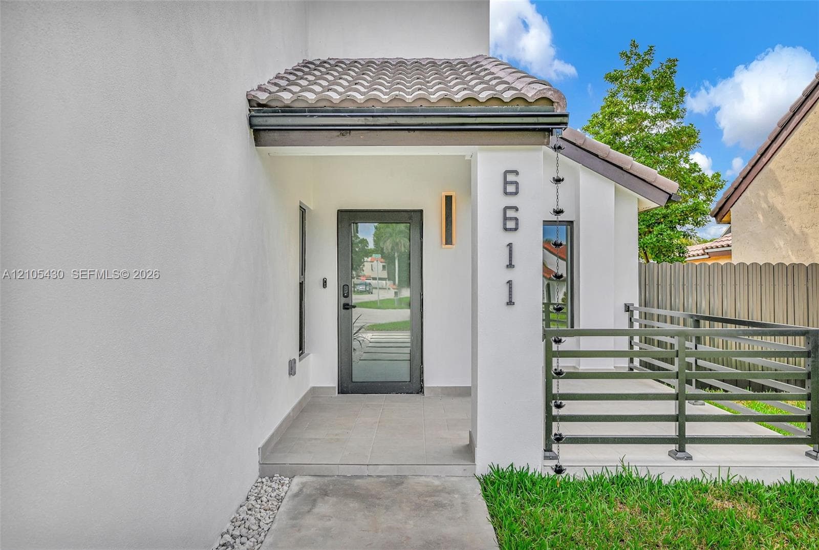 Covered entryway featuring a tiled porch, glass-panel door, metal chain downspout, and modern horizontal-slat railings