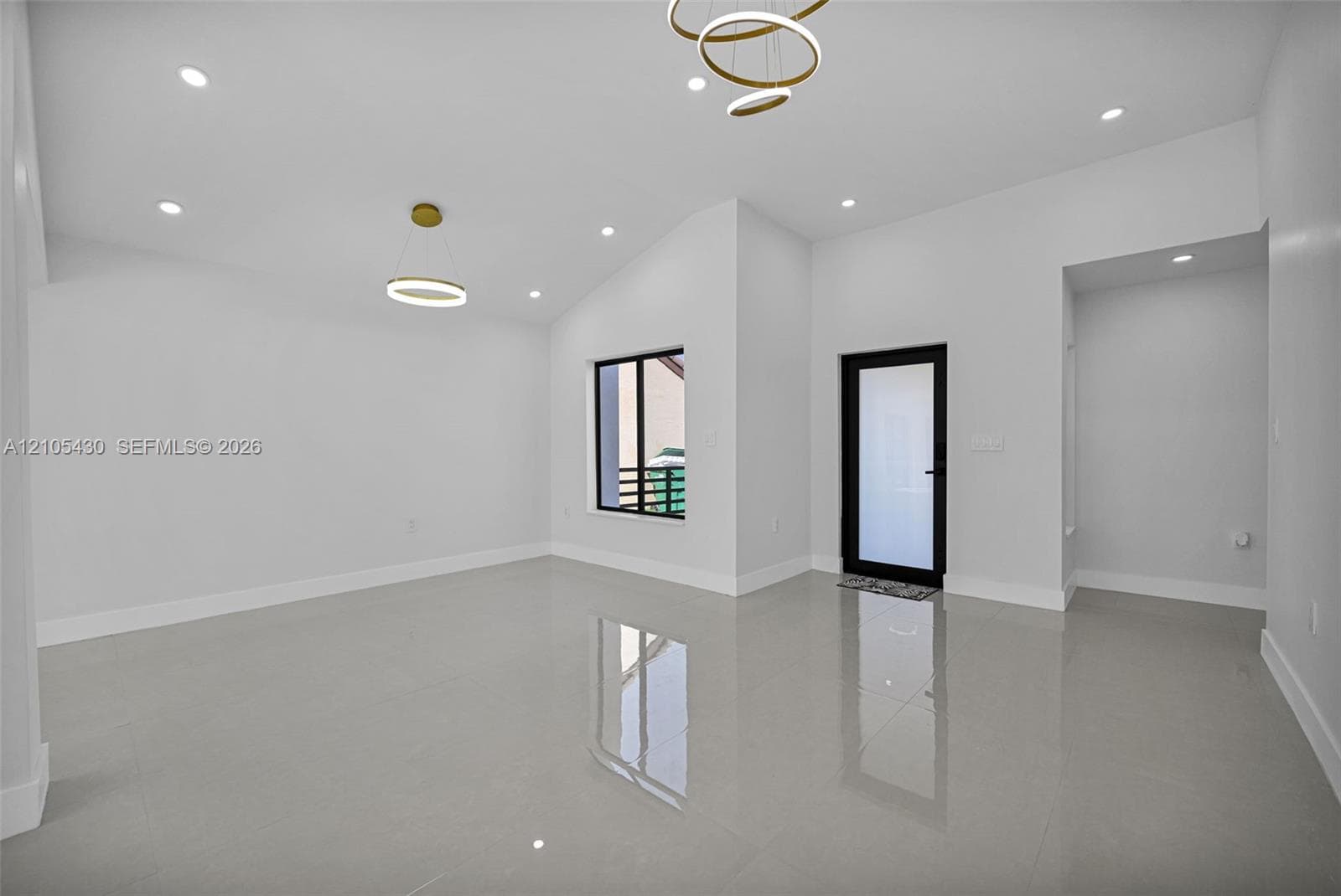 High-ceiling interior featuring glossy tile flooring, recessed lighting, modern geometric pendant fixtures, and a glass-paneled entry door with a matte black frame