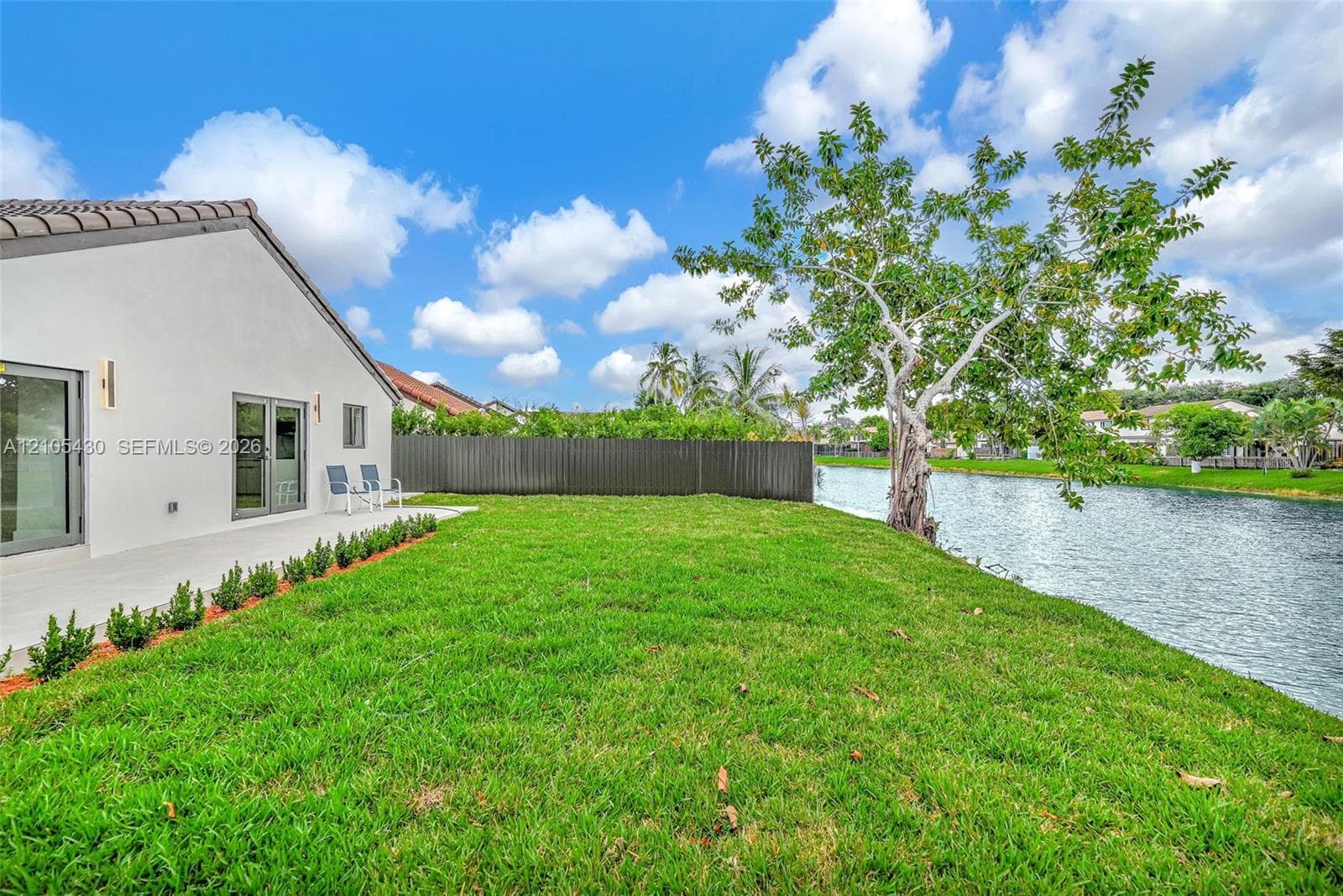 Backyard featuring a concrete patio, manicured lawn, perimeter fencing, and direct waterfront access