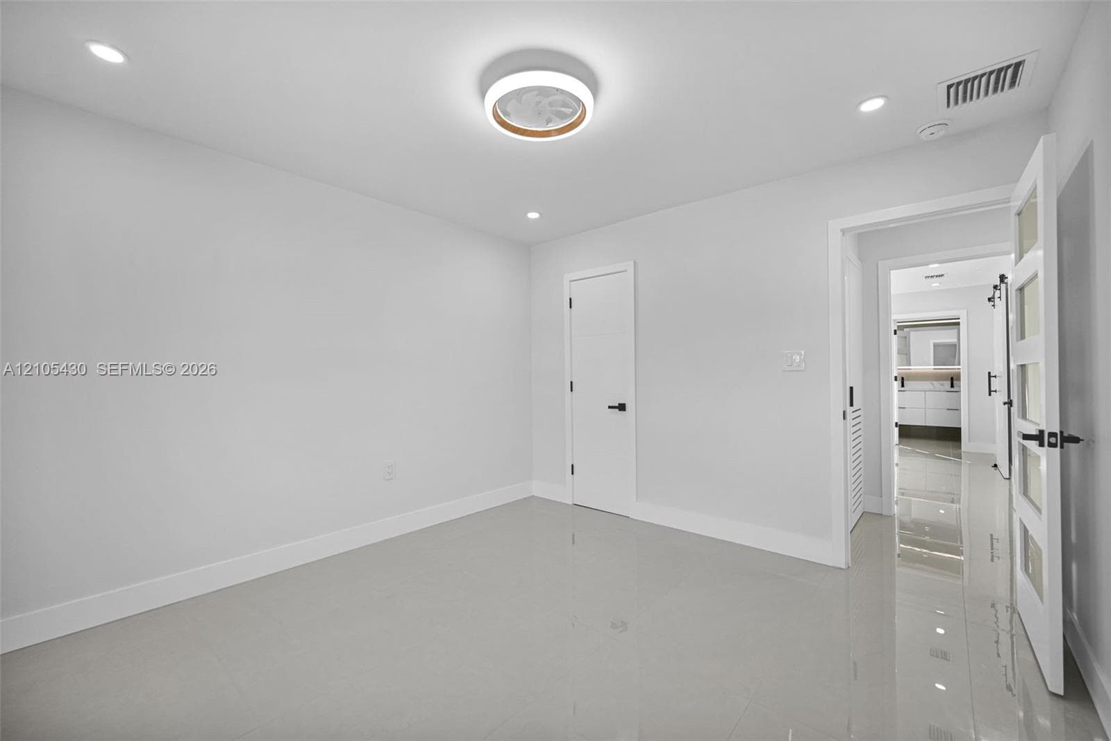Interior room featuring polished tile flooring, recessed lighting, a modern circular flush-mount ceiling fixture, and a four-panel frosted glass door with matte black hardware