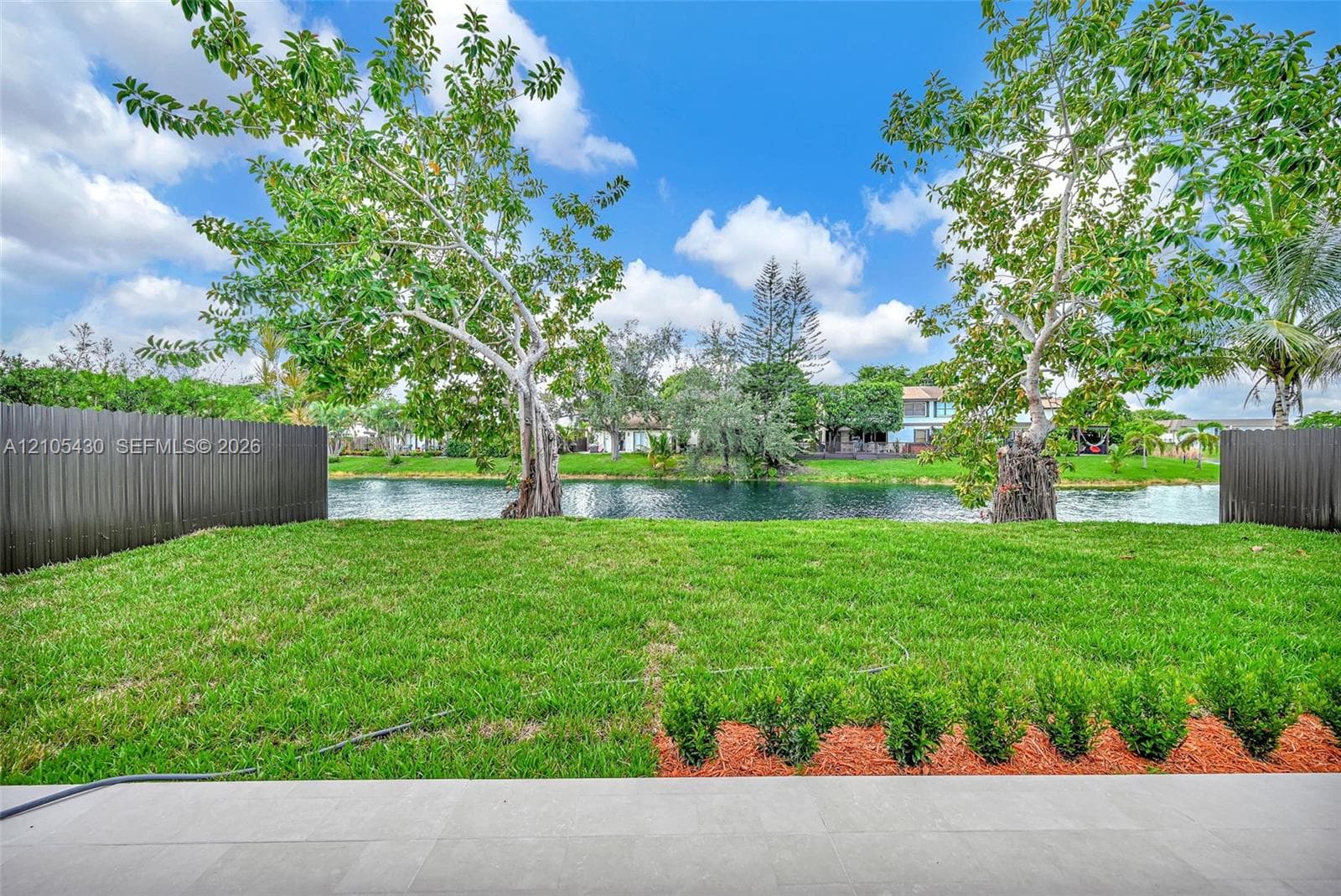 Backyard featuring a paved stone patio, expansive grass lawn, perimeter privacy fencing, and direct water frontage