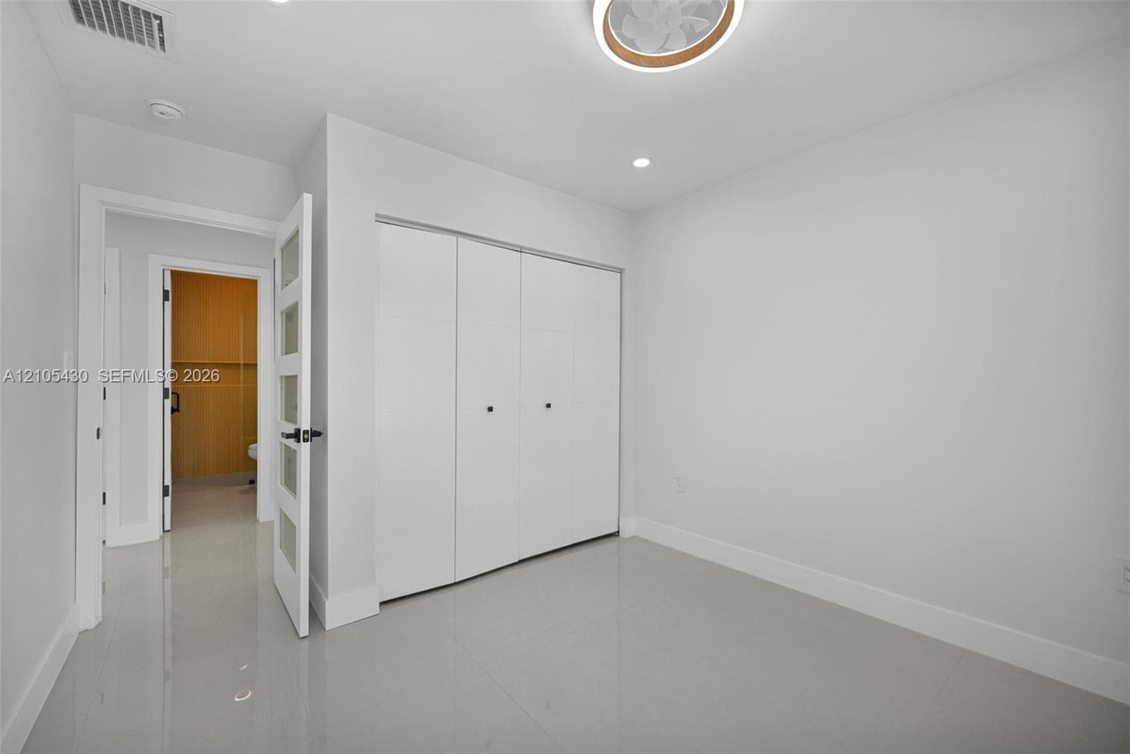 Neutral-toned interior space featuring light-colored tile flooring, a recessed ceiling fan, and a three-panel sliding closet