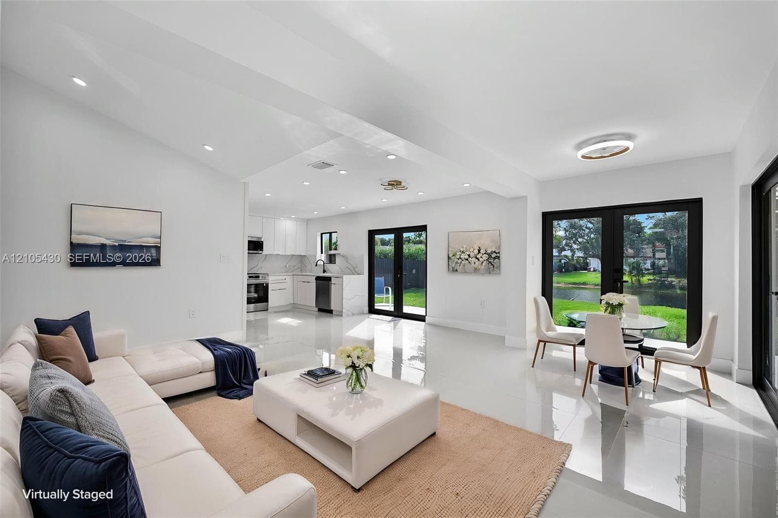 Open-concept living space featuring high-gloss tile flooring, recessed lighting, kitchen cabinetry with stone-surfaced countertops, and black-framed French doors opening to an exterior waterfront area