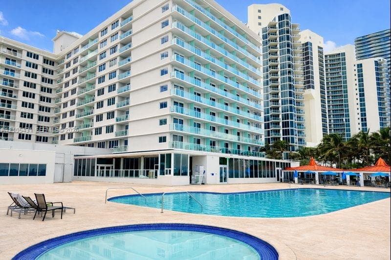 Resort-style pool area featuring a large swimming pool, circular hot tub, and expansive paver deck