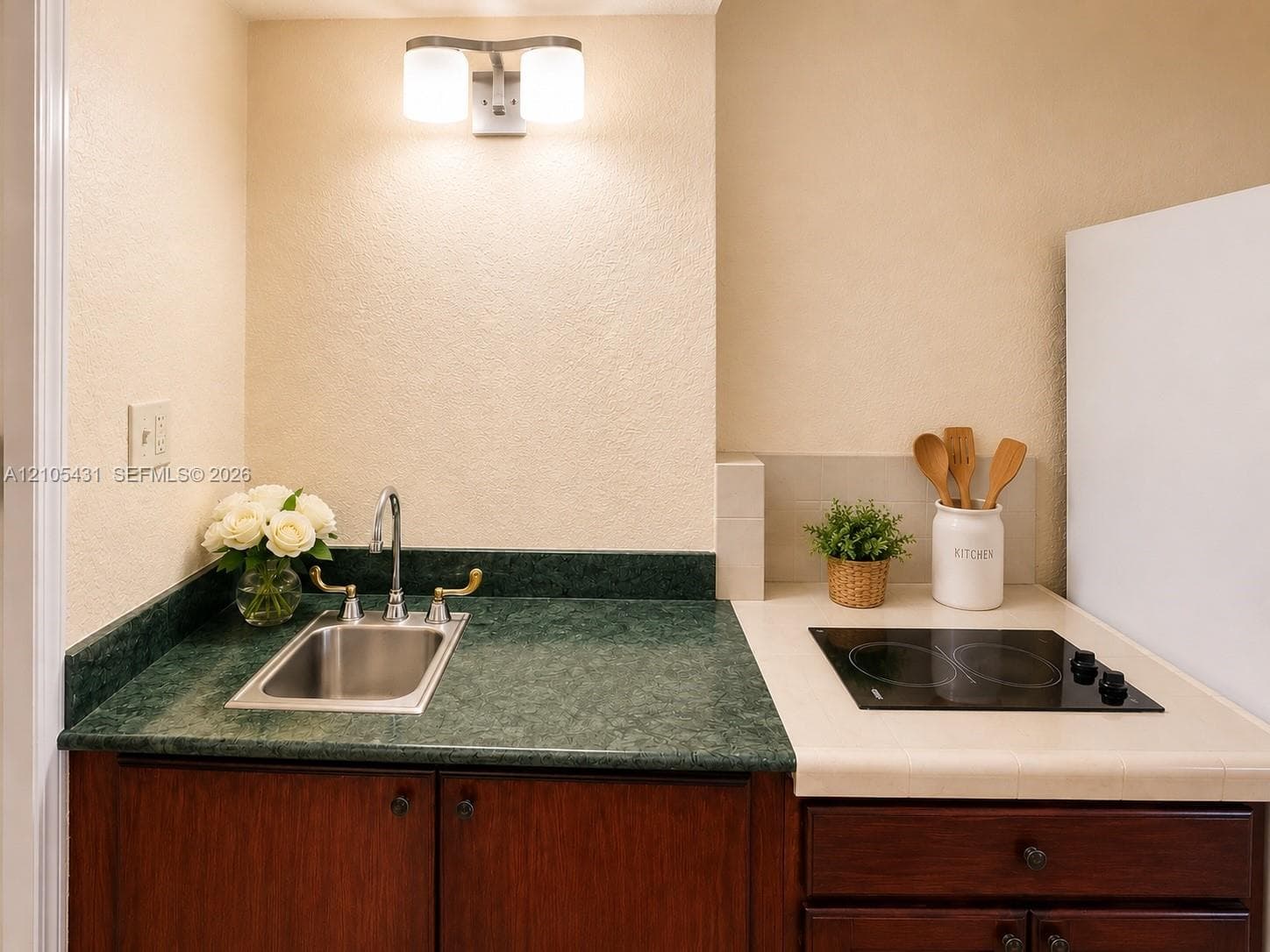 Compact kitchenette featuring a stainless steel sink, dark wood-finish cabinetry, green stone-look countertop, and a built-in electric cooktop
