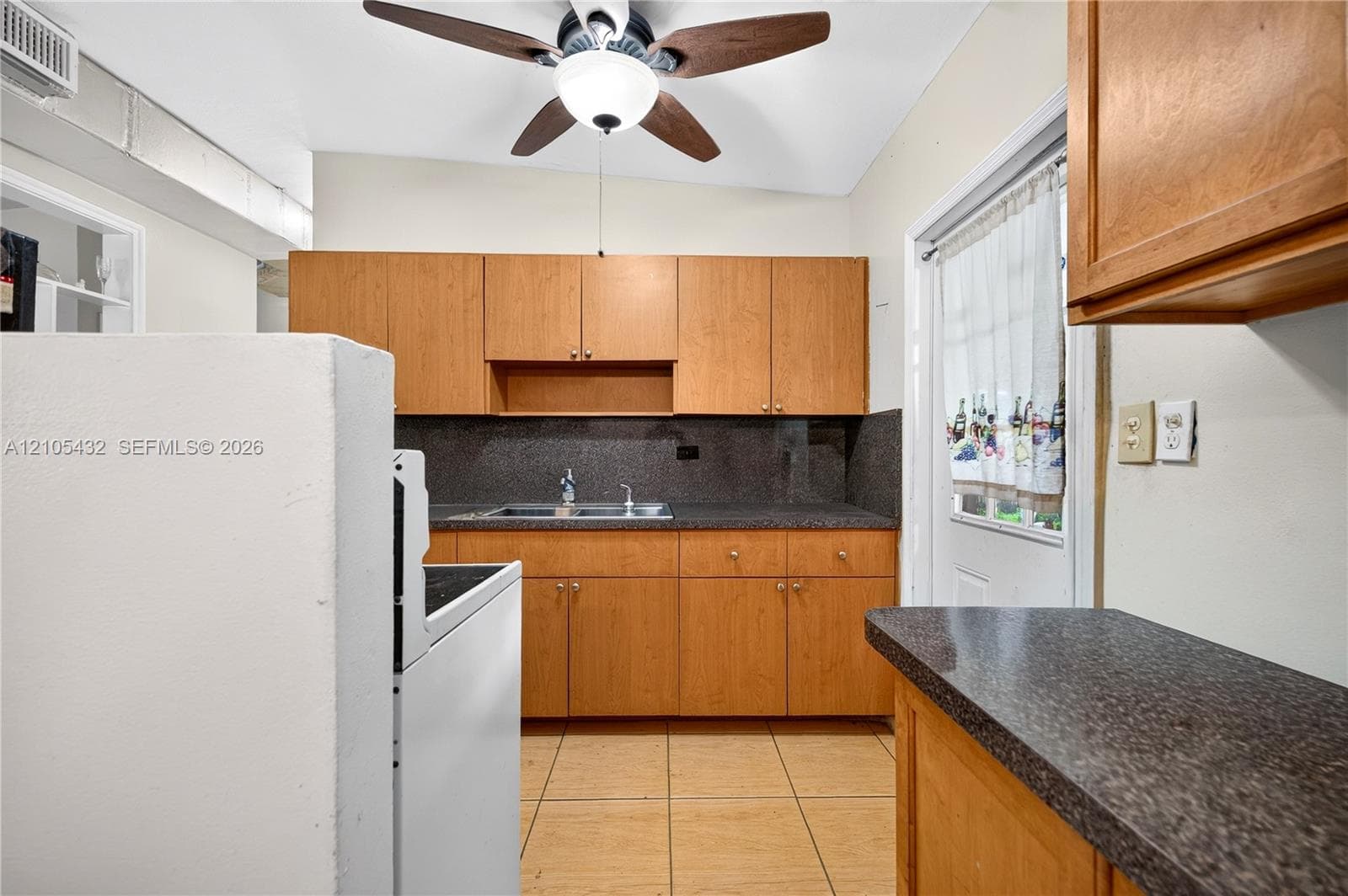 Kitchen featuring wooden cabinetry, dark stone-finish countertops, ceramic tile flooring, and a ceiling-mounted light fixture with integrated fan