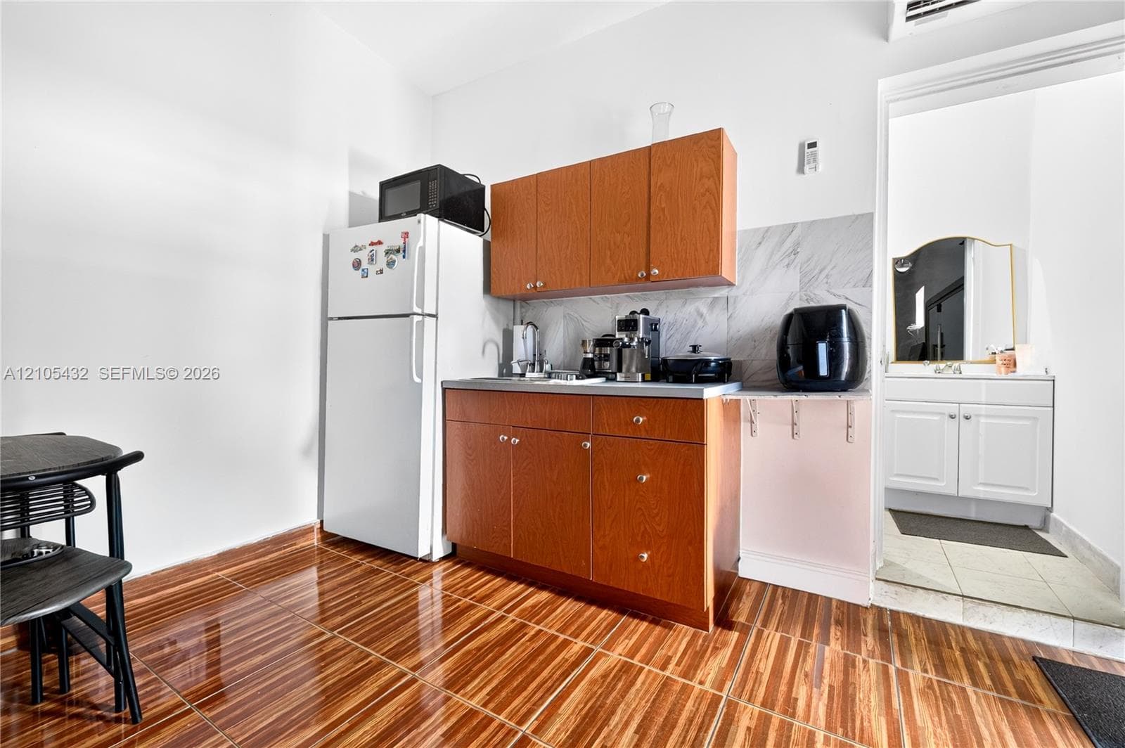 Kitchenette featuring wood-finish cabinetry, a stone-pattern backsplash, and glossy tile flooring