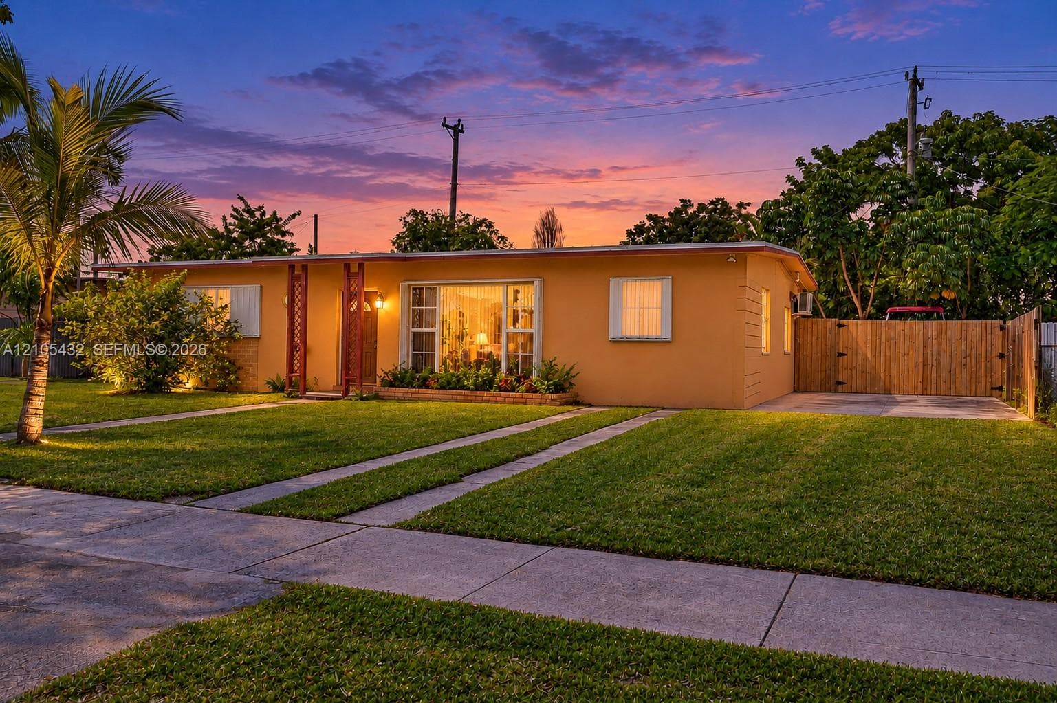 Single-story residence featuring a stucco exterior, expansive front lawn, paved dual-strip driveway, and a wooden privacy fence