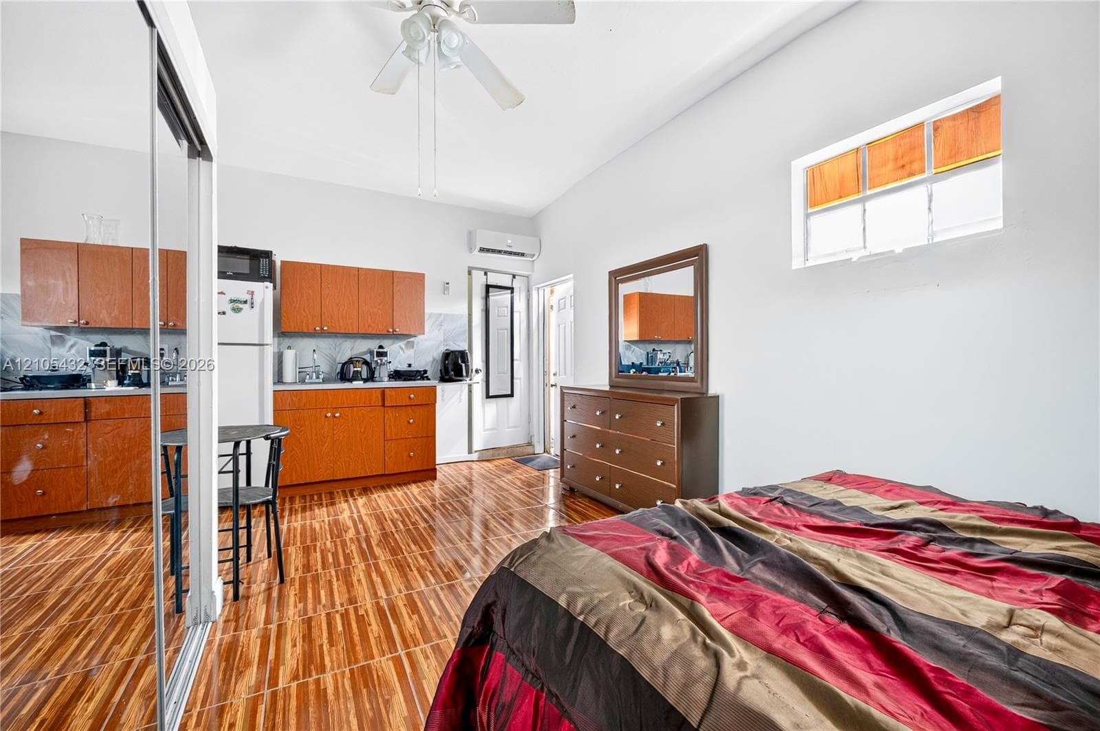 Wood-finish tile flooring, wood-toned cabinetry, ceiling fan, wall-mounted air conditioning unit, and sliding mirrored closet doors