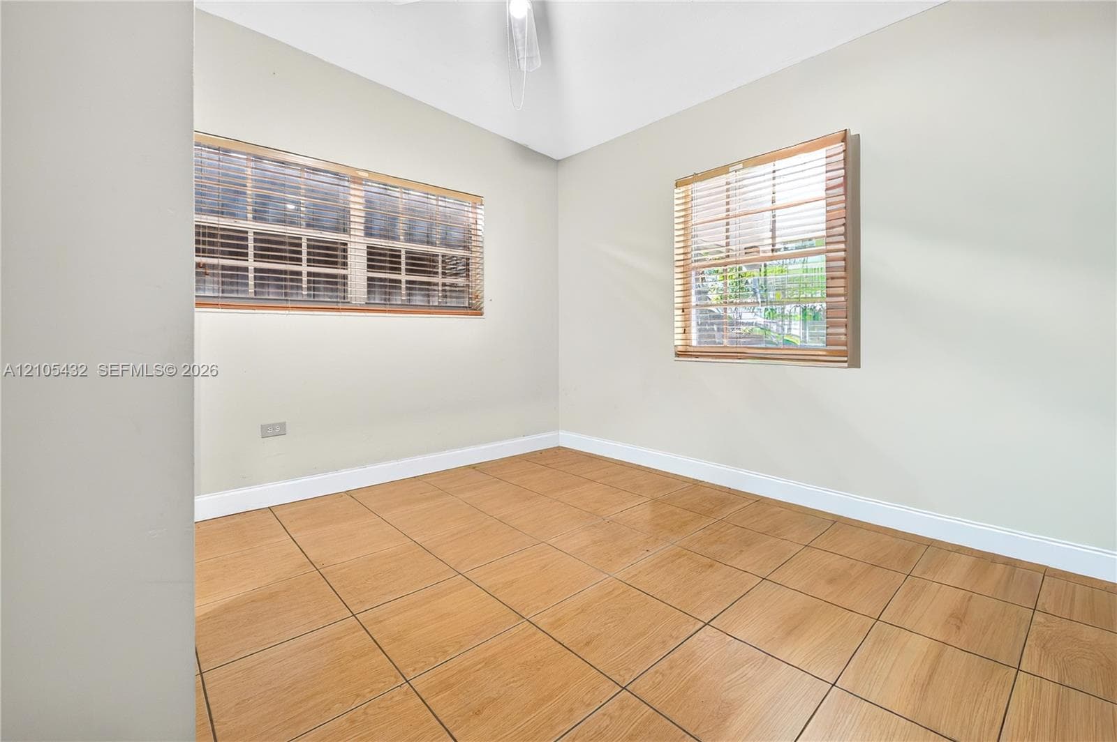 Neutral-toned interior featuring wood-finish tile flooring, vaulted ceilings, and dual windows equipped with horizontal blinds