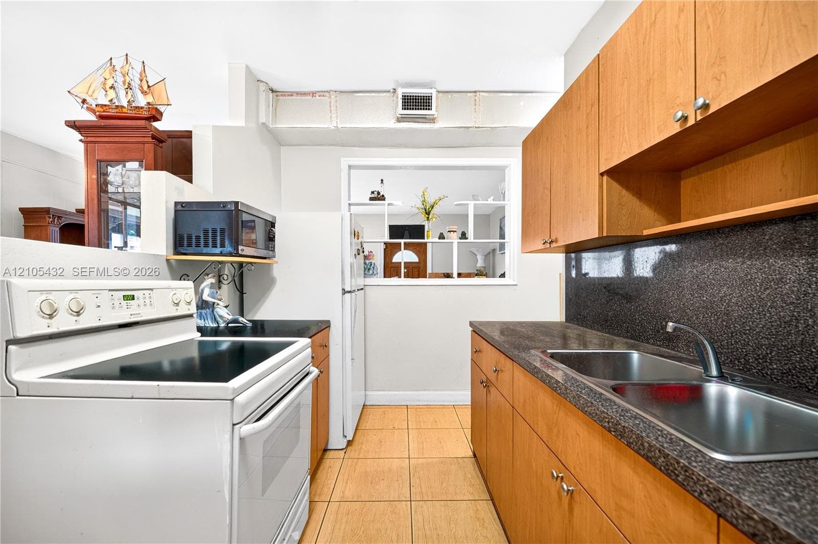 Kitchen featuring light wood cabinetry, dark stone-finish countertops, dual-basin stainless steel sink, and ceramic tile flooring