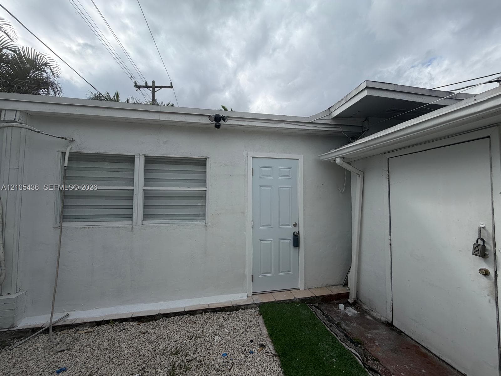 Exterior elevation featuring a light-colored stucco finish, multi-pane casement windows, a paneled entry door, and a low-maintenance ground cover comprising gravel and turf