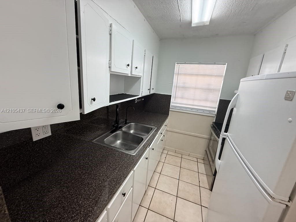 Kitchen featuring white cabinetry, dark speckled countertops, a double-basin stainless steel sink, and tile flooring