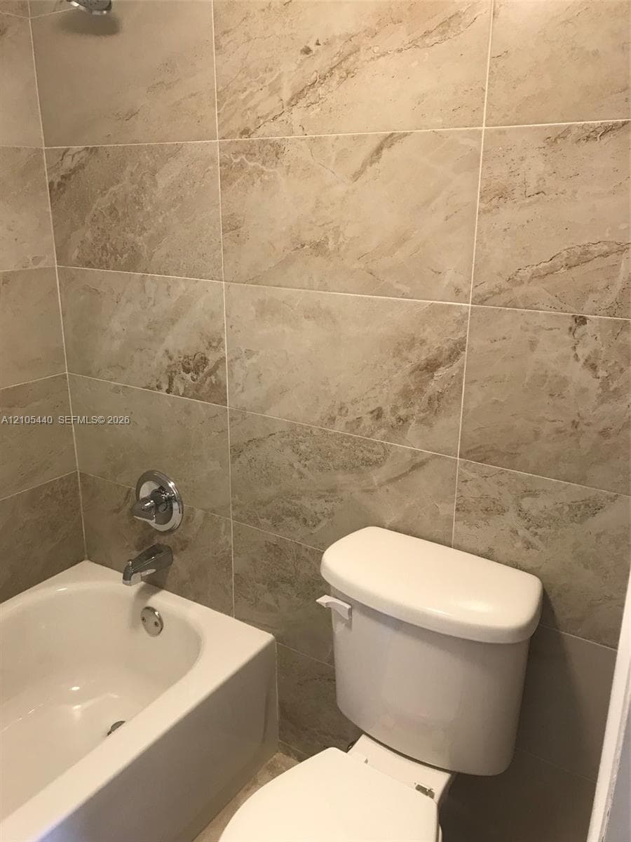 Bathroom featuring a built-in bathtub, chrome fixtures, and neutral-toned wall tiles