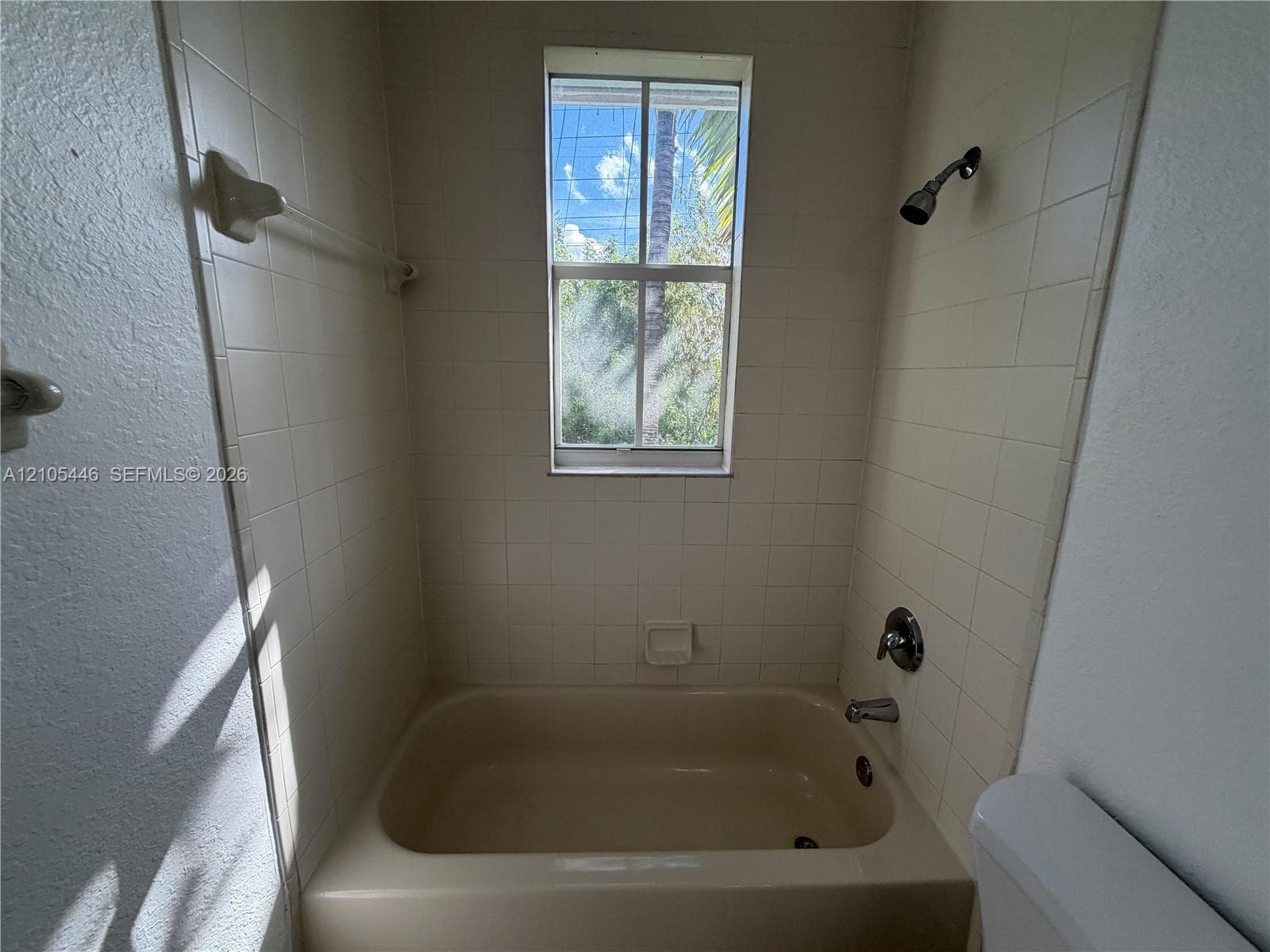 Bathroom featuring a vanity with an integrated sink, a large wall-mounted mirror, a four-bulb vanity light fixture, a toilet, and a bathtub with a shower