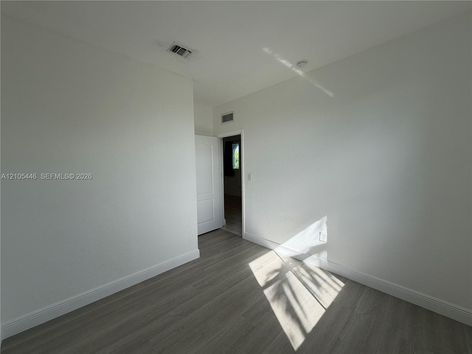 Light-toned wood-finish flooring, white walls, and a window with a black curtain rod
