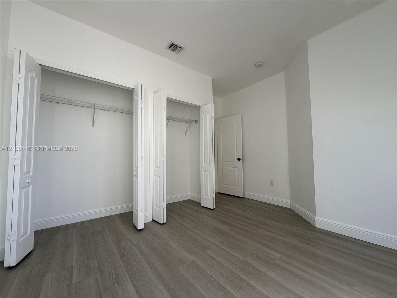 Wood-finish flooring, white painted walls, and window treatments with dark rods