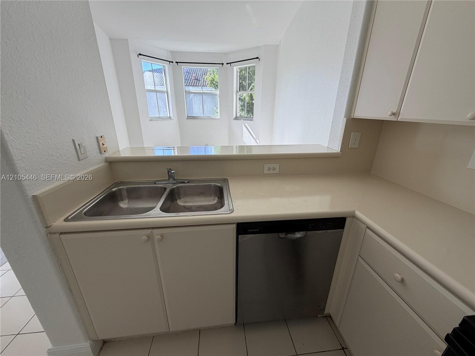 Kitchen featuring white cabinetry, light-toned countertops, a stainless steel microwave, a stainless steel and black range, and white tiled flooring
