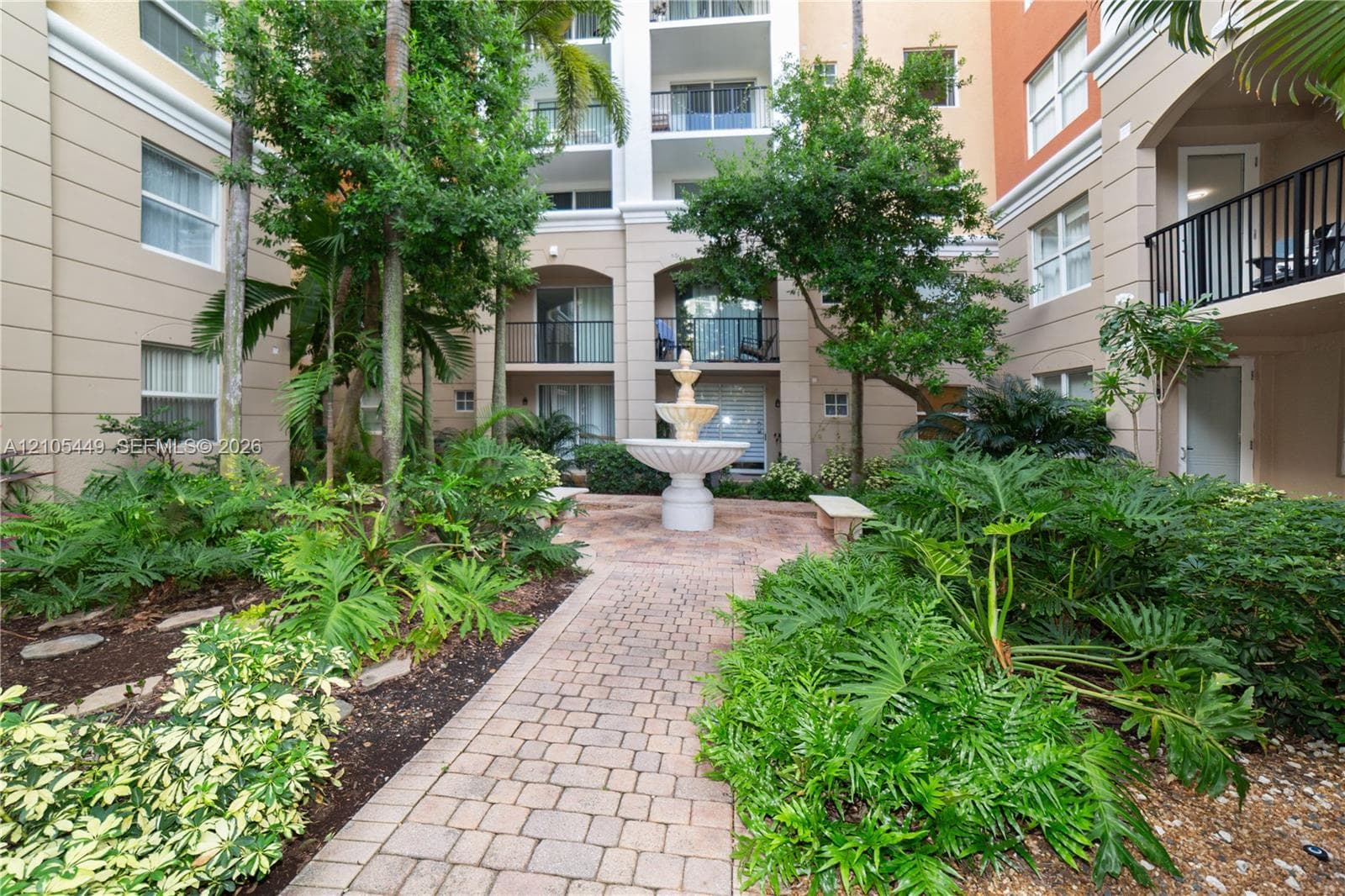 Central courtyard featuring a tiered fountain, paver walkway, lush landscaping, and mature trees