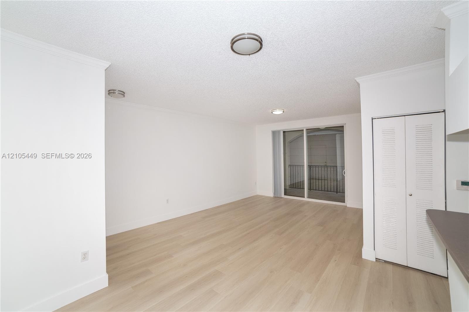 Light wood-finish flooring, white walls, crown molding, and sliding glass doors to a balcony