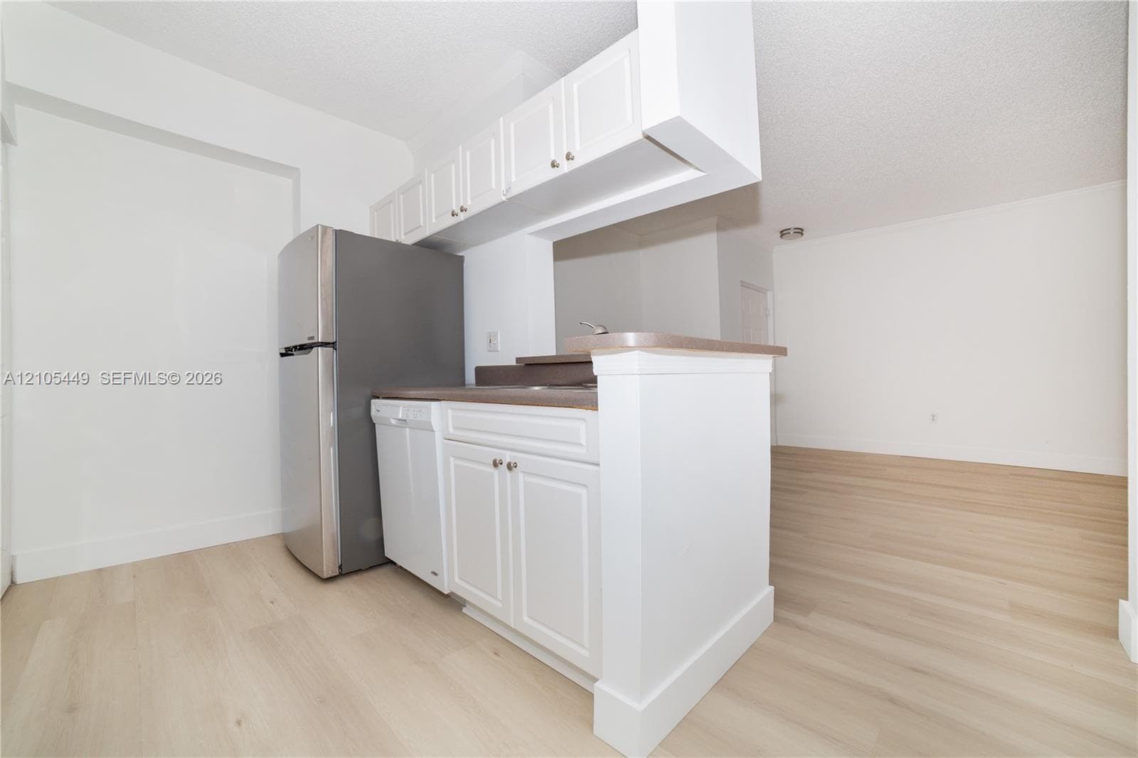 White cabinetry with brushed nickel hardware, stainless steel refrigerator, integrated dishwasher, and wood-finish flooring