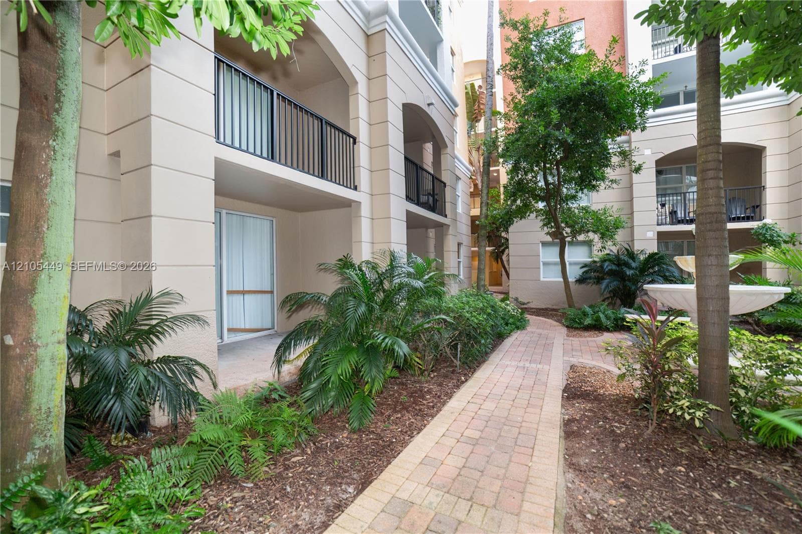 Paved walkway leading to a private ground-level patio, surrounded by lush landscaping and mature trees