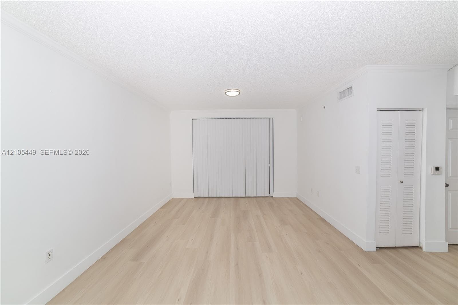 Expansive room featuring wood-finish flooring, white walls, vertical blinds, and a flush-mount ceiling light