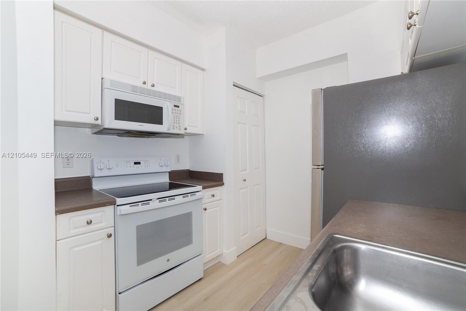 Kitchen featuring white cabinetry, a stainless steel sink, an electric range, an over-the-range microwave, and light wood-finish flooring