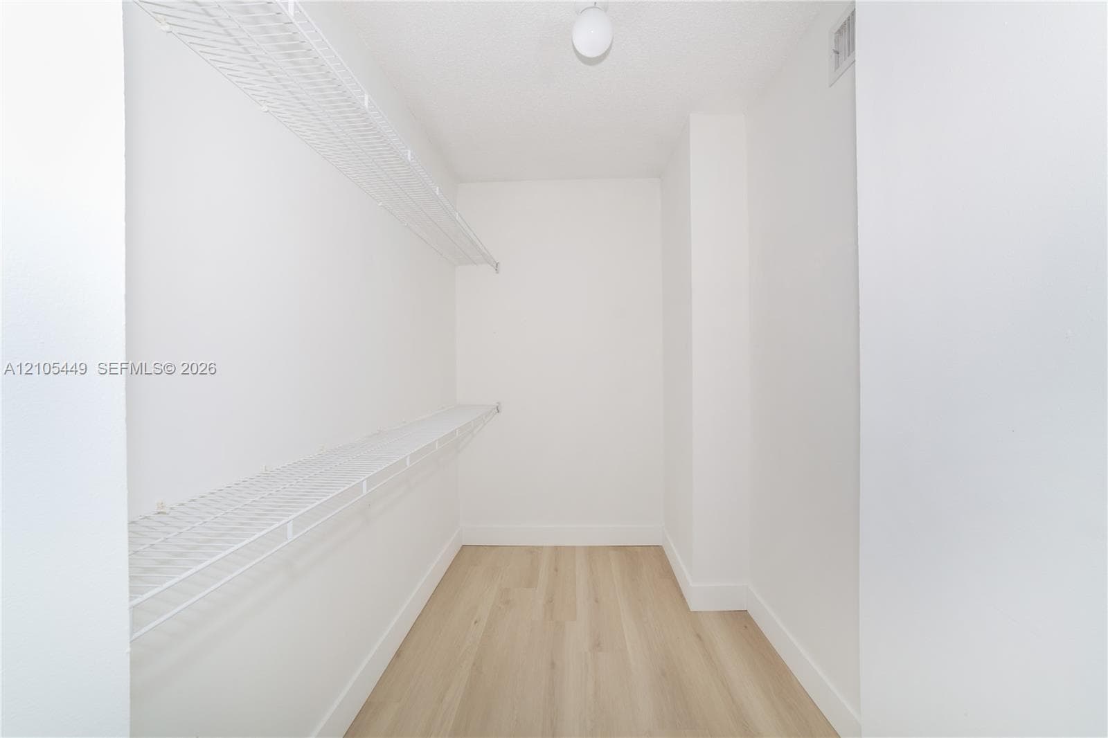 Light wood-finish flooring with white baseboards, white walls, and built-in wire shelving