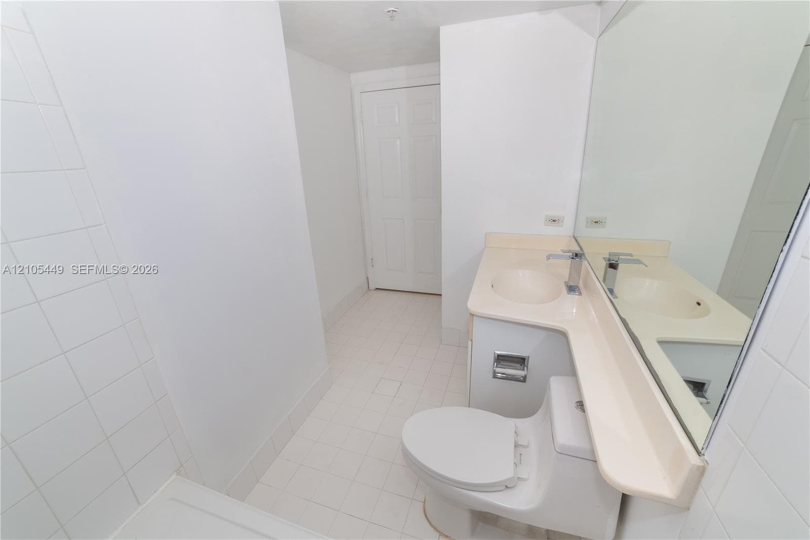 White tile flooring, white tile shower surround, integrated sink vanity with a light-colored countertop, and a large wall-mounted mirror