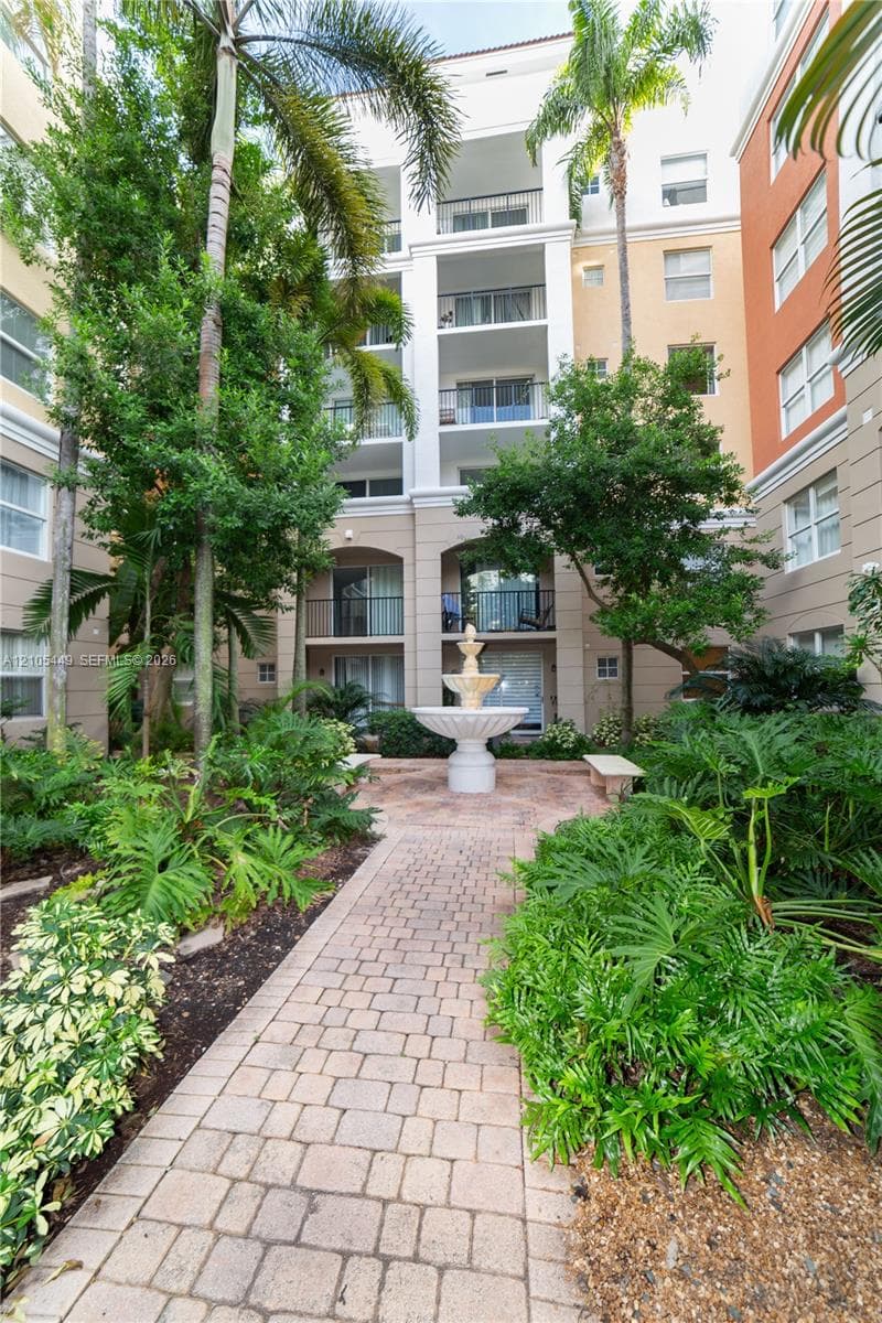 Paver pathway leading to a central water feature fountain, surrounded by lush landscaping and mature palm trees