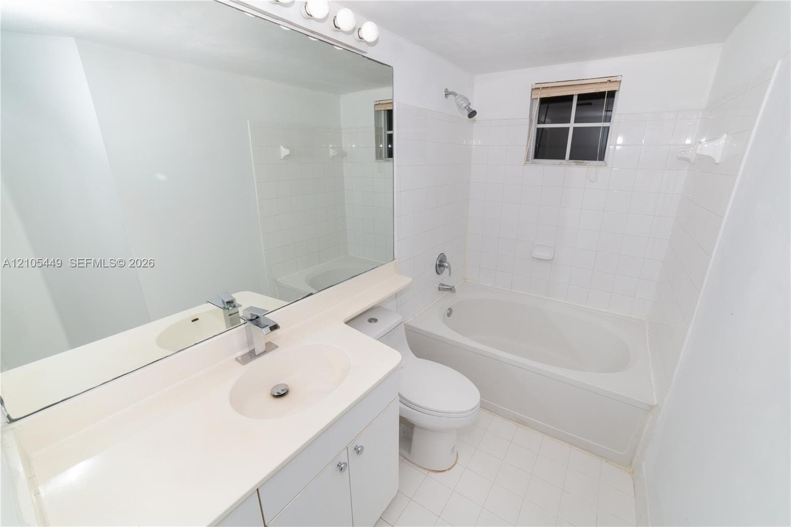 Full vanity mirror with overhead lighting, single basin sink with chrome faucet, full bathtub with shower, and white tiled walls