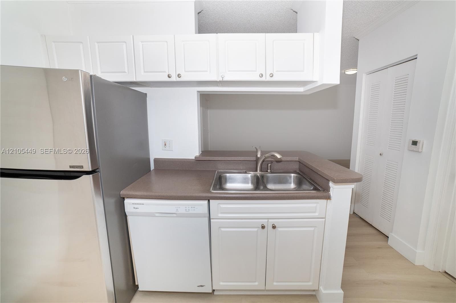 Kitchen featuring white upper and lower cabinetry, stainless steel refrigerator, white dishwasher, and a double basin sink with a gooseneck faucet