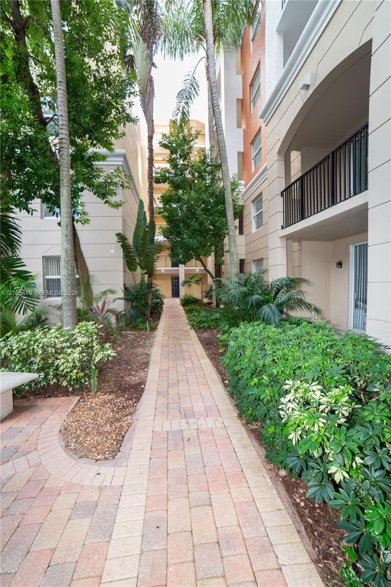 Paver pathway bordered by lush landscaping and mature palm trees