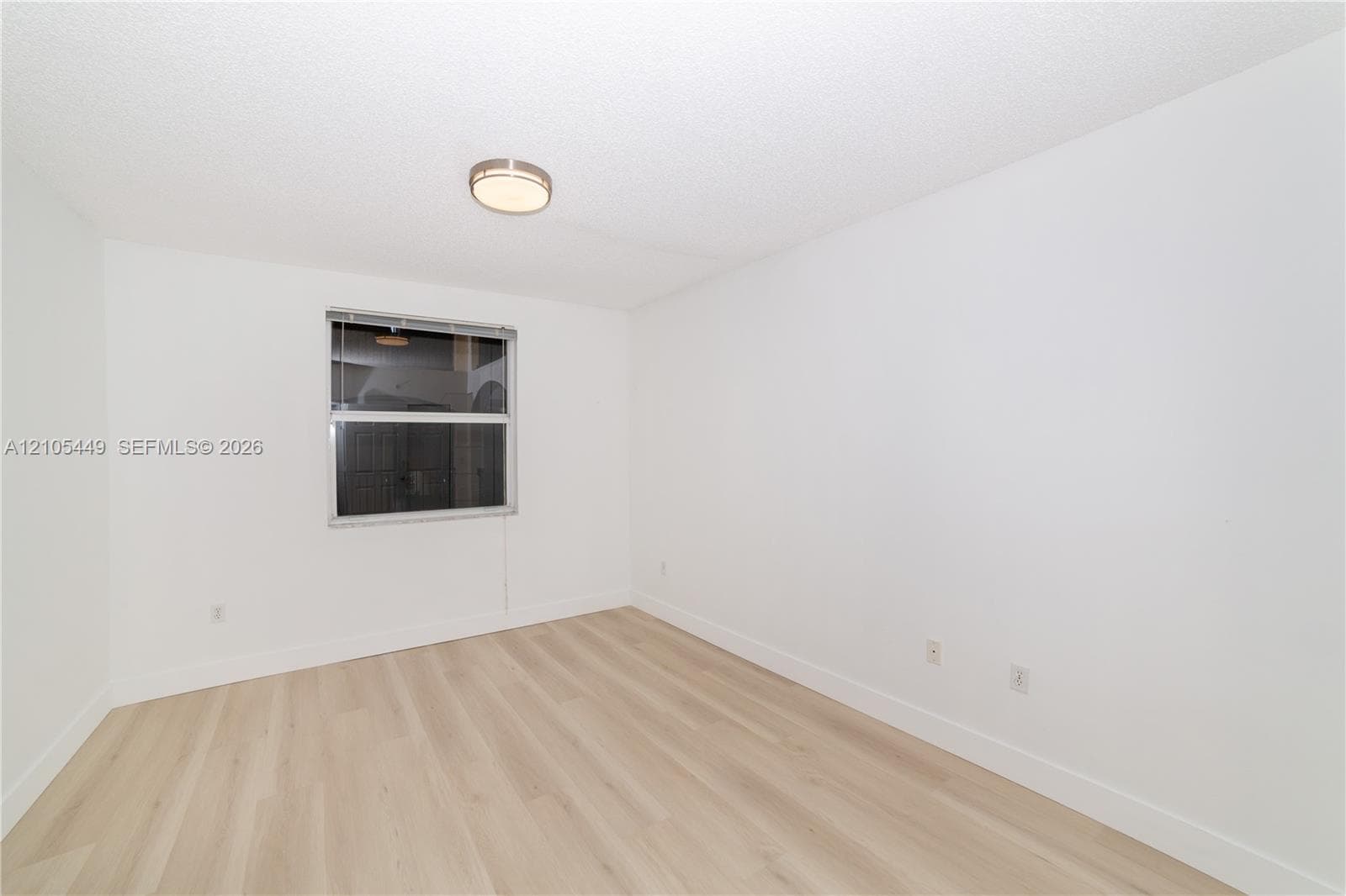 White walls, wood-finish flooring, and a single window with blinds