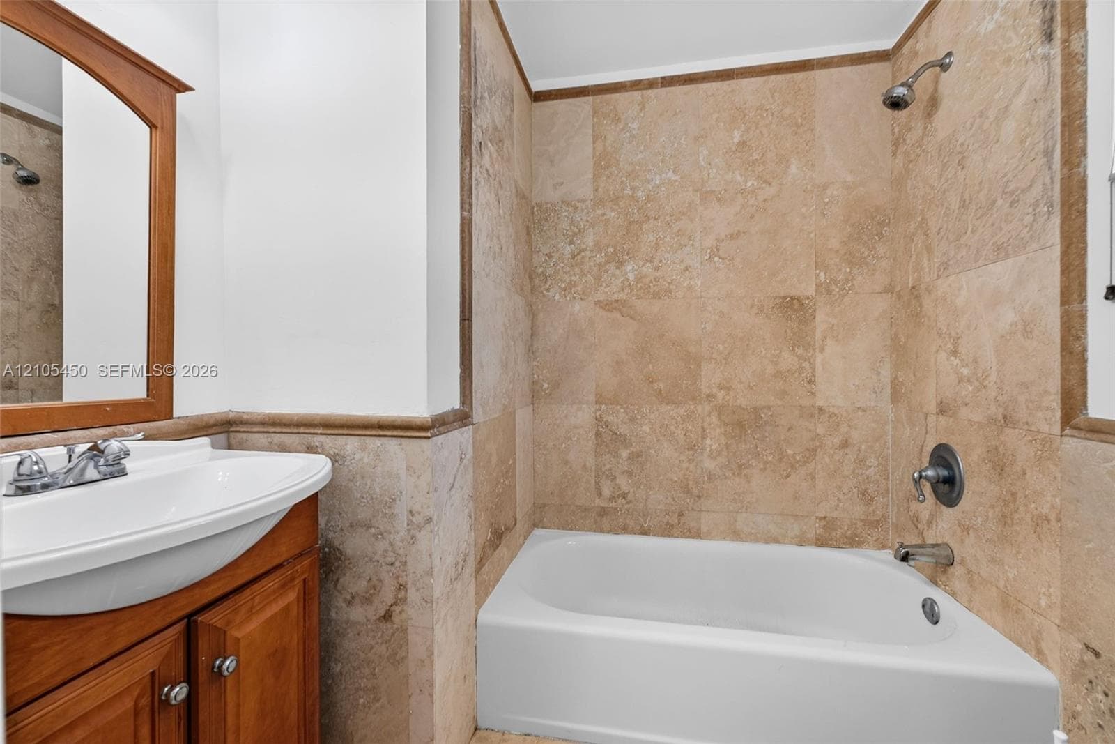 Bathroom featuring a white drop-in tub, tiled shower surround, integrated sink, and a wood-finish vanity with cabinet storage