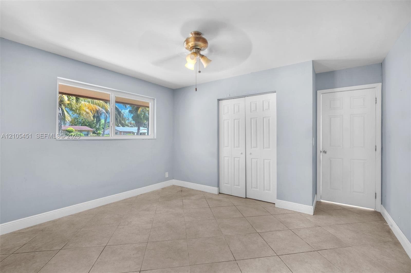 Room featuring large-format ceramic tile flooring, a dual-pane horizontal sliding window, a six-panel closet with bi-fold doors, a six-panel interior door, and a ceiling fan with integrated lighting