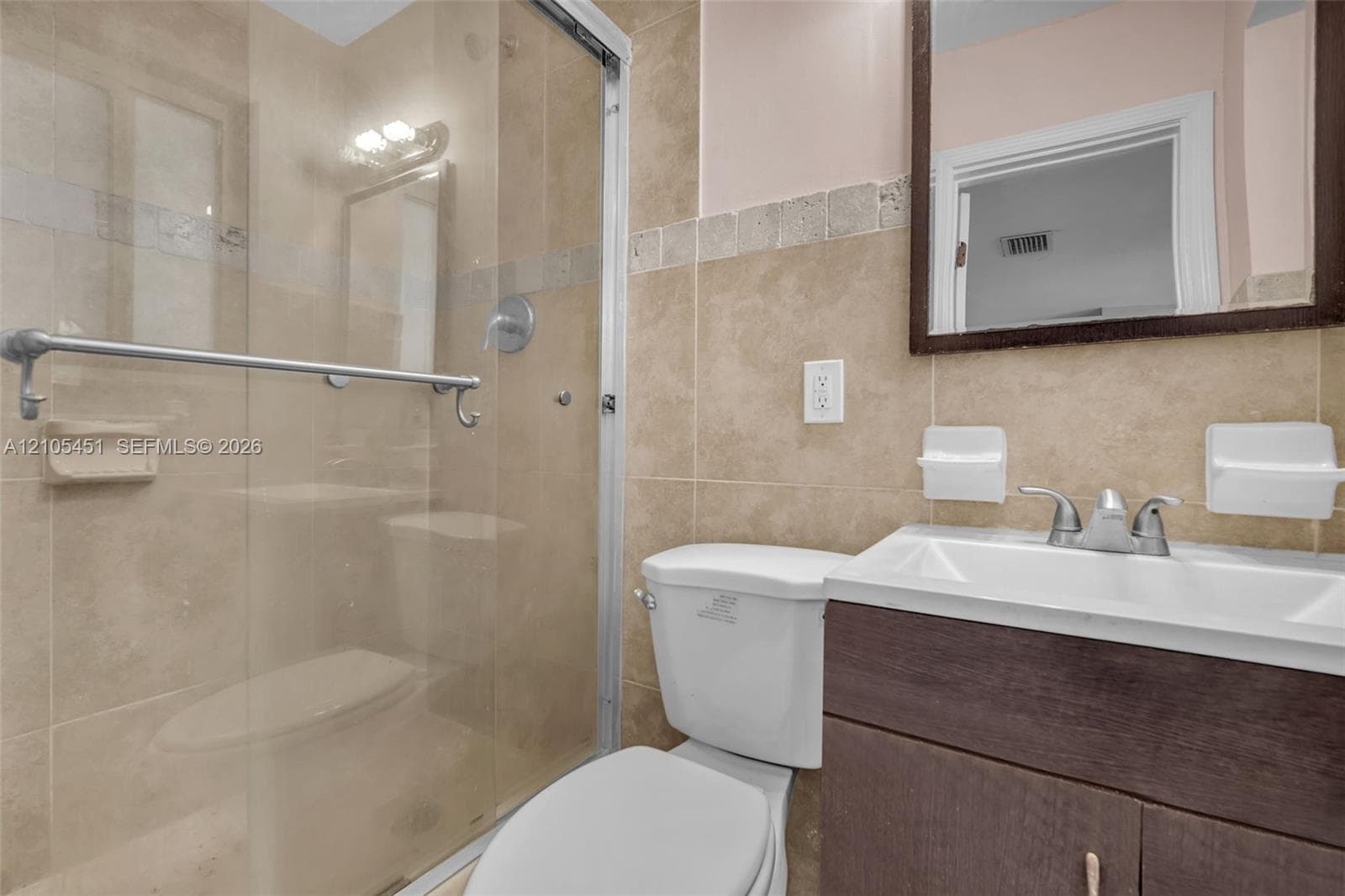 Bathroom featuring a dark wood-finish vanity, white rectangular sink with dual-handle faucet, and a glass-enclosed shower with neutral-toned wall tile