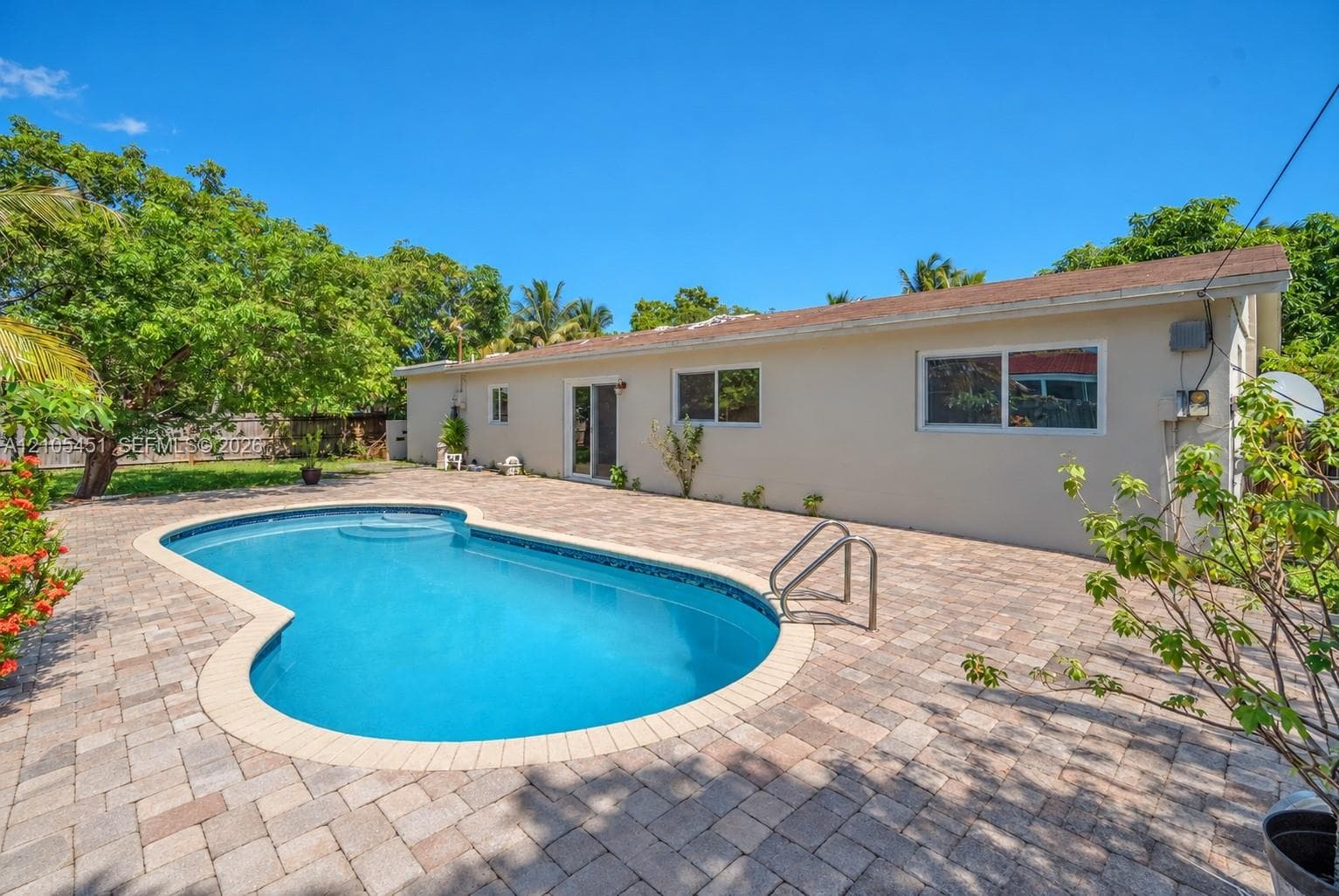 In-ground pool surrounded by expansive paver patio, set against a backdrop of mature trees and privacy fencing