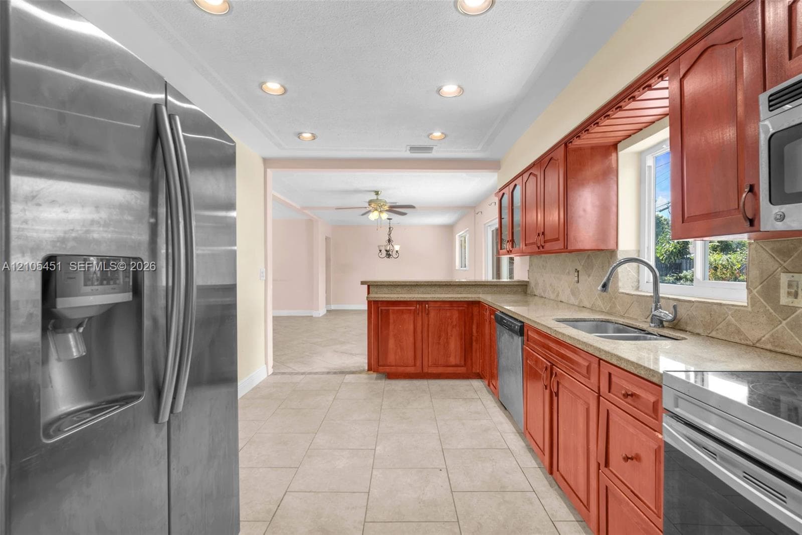 Kitchen featuring cherry-finish cabinetry, stone-surface countertops, stainless steel appliances, tile flooring, and recessed lighting