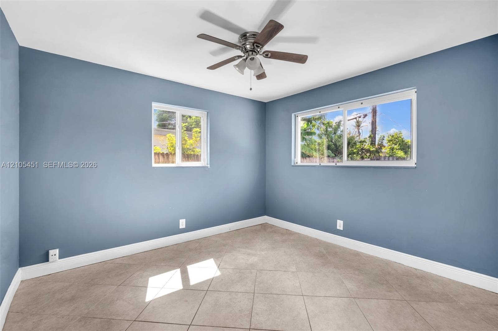 Room featuring tile flooring, neutral wall paint, two sliding windows, and a multi-blade ceiling fan with integrated lighting