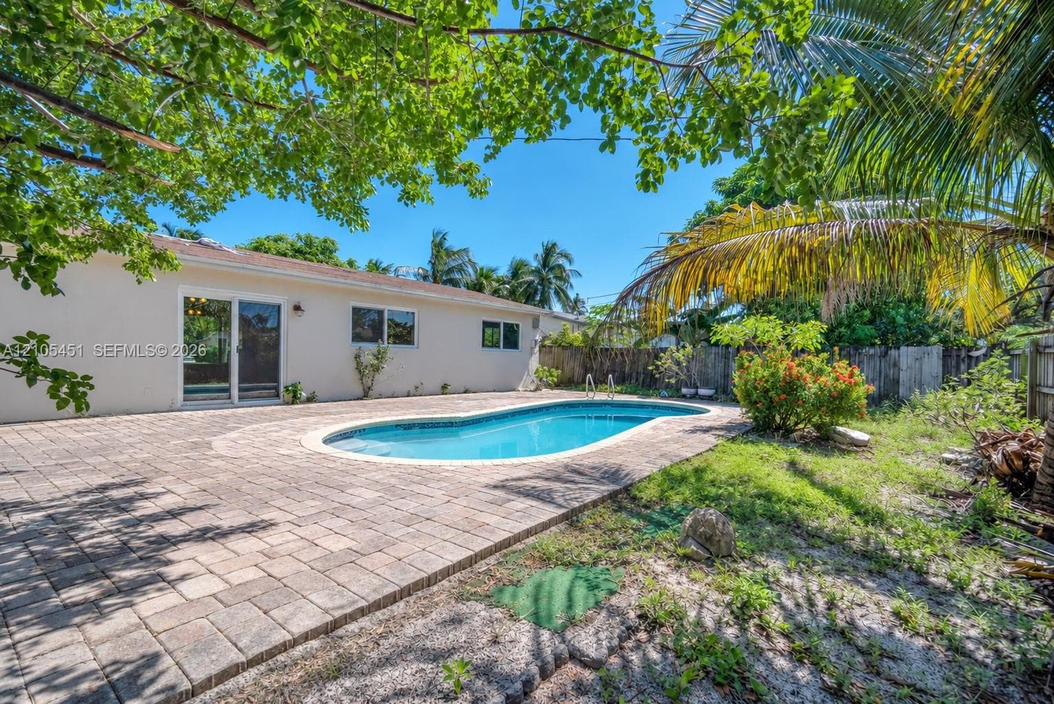 Backyard featuring an in-ground swimming pool, expansive paver patio, wood-style fencing, and mature tropical landscaping