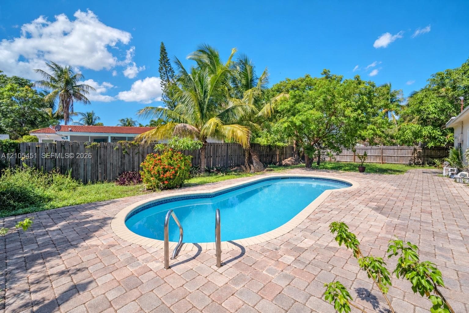 Backyard featuring an in-ground swimming pool, brick paver patio, wood fence, and mature palm trees