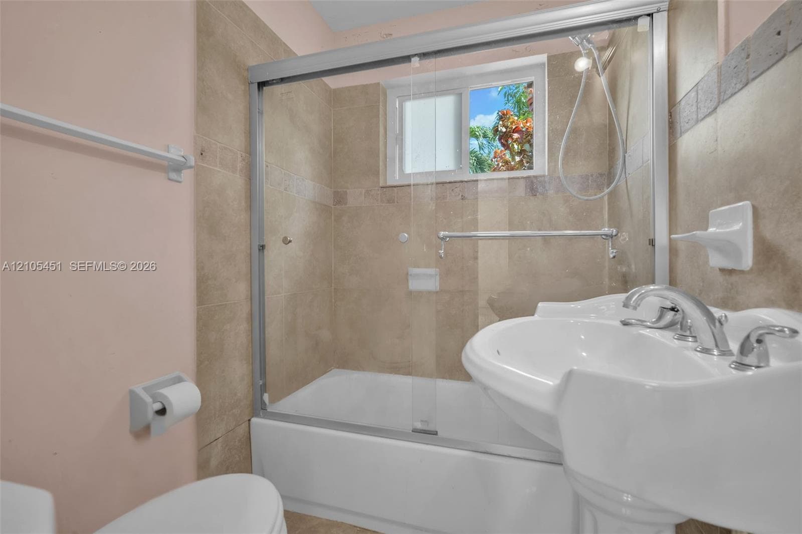 Bathroom featuring a porcelain pedestal sink with polished chrome fixtures, a combination tub and shower with sliding glass doors, and floor-to-ceiling tile surround